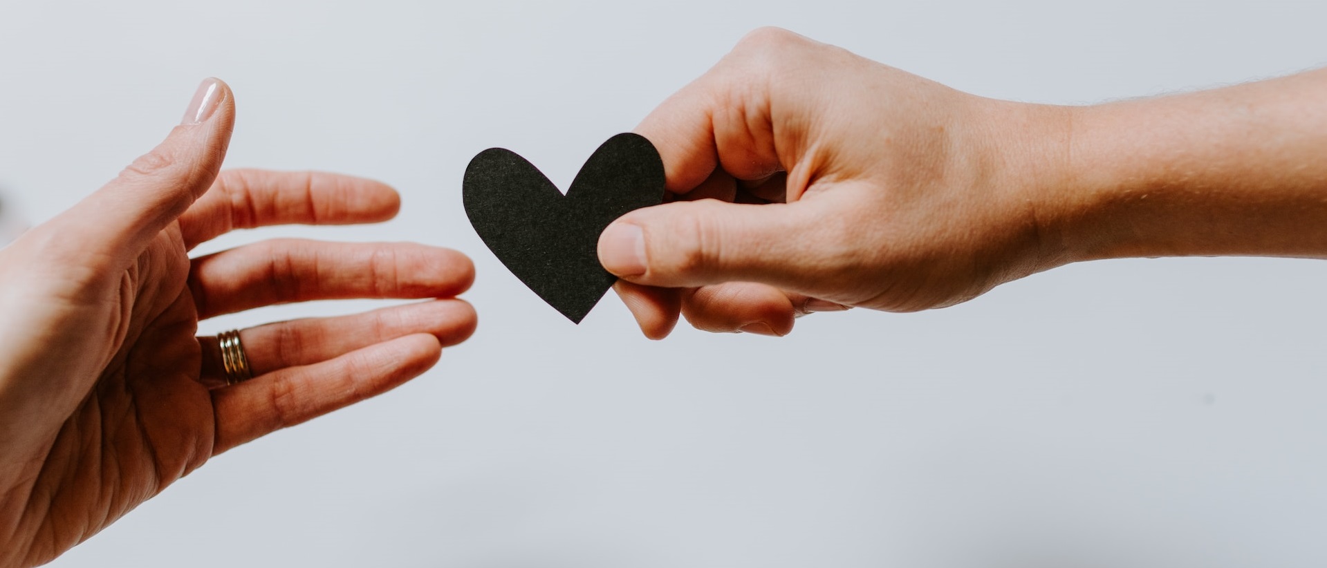 A photograph of a hand handing another hand a paper heart